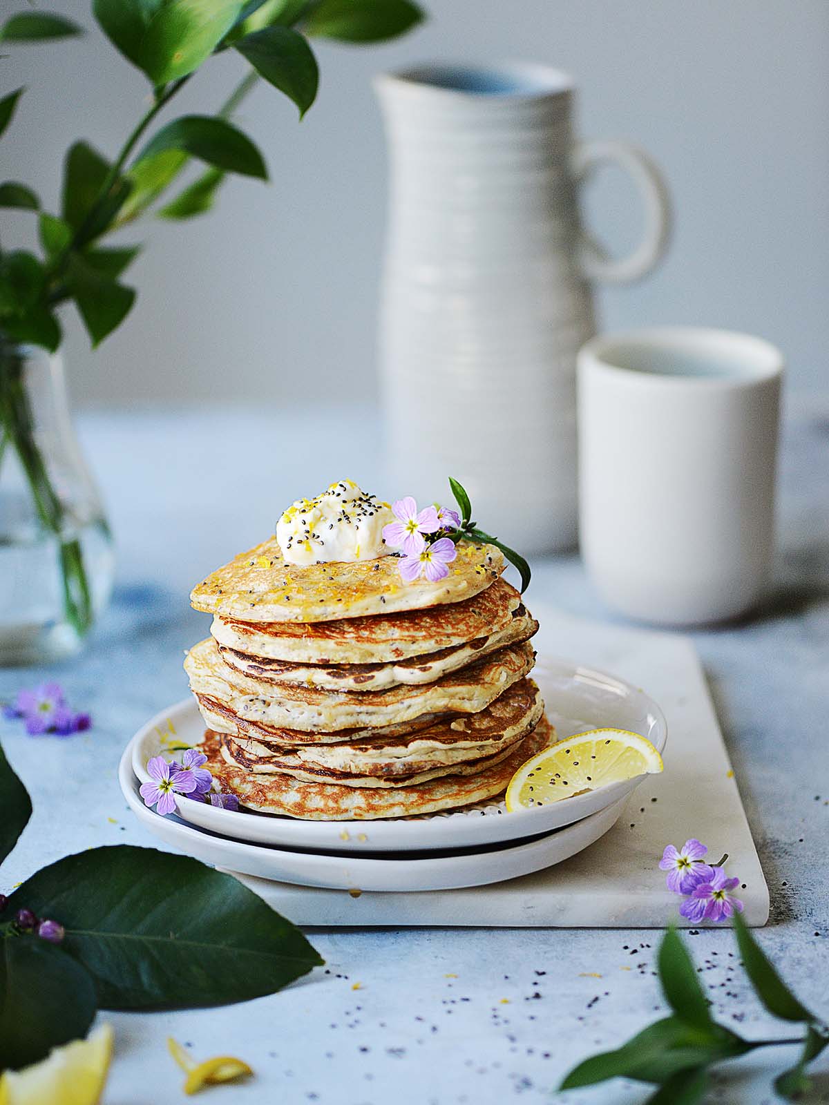 A stack of lemon protein pancakes with a jar and a mug in the background.