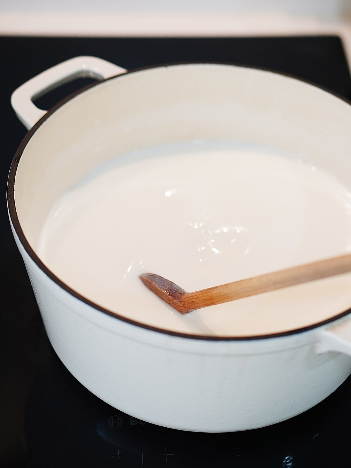 Cooking the milk in a large white sauce pot and mixing it with a wooden spoon.