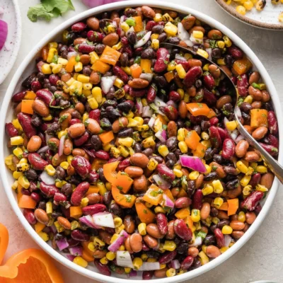 A bowl with bean salad with a spoon in it.