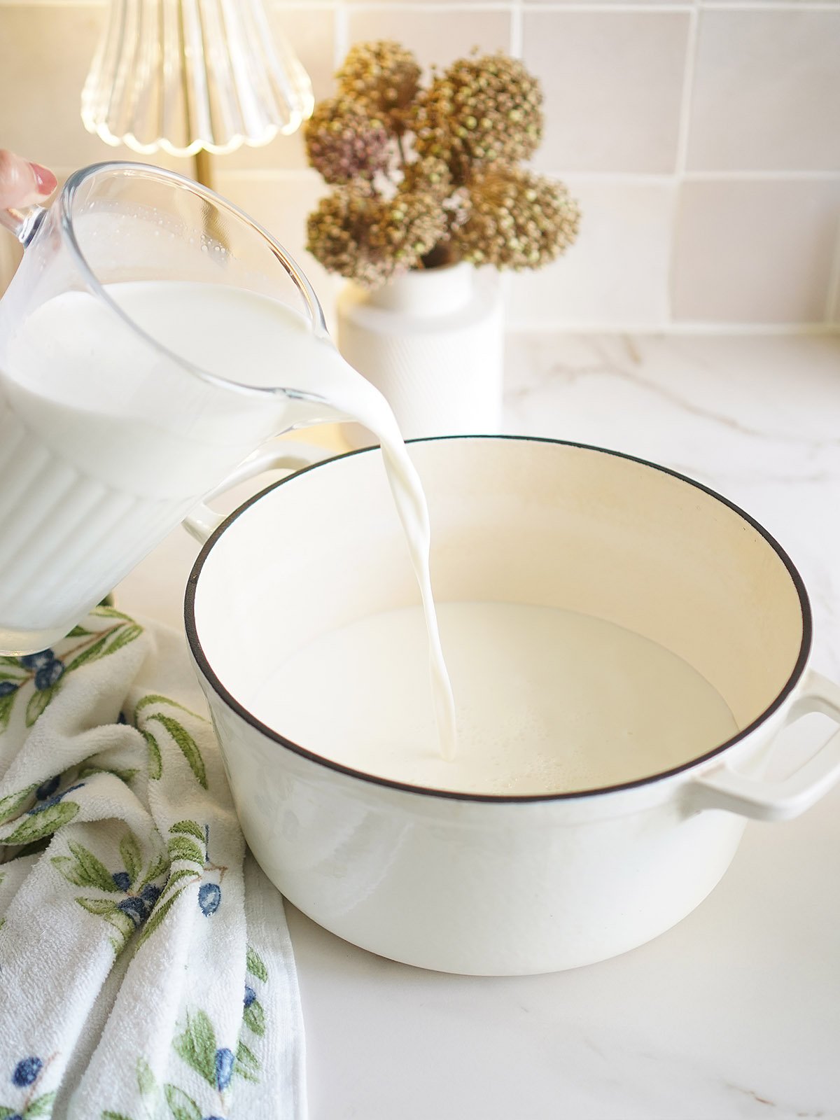 Pouring the milk into a large white sauce pot.