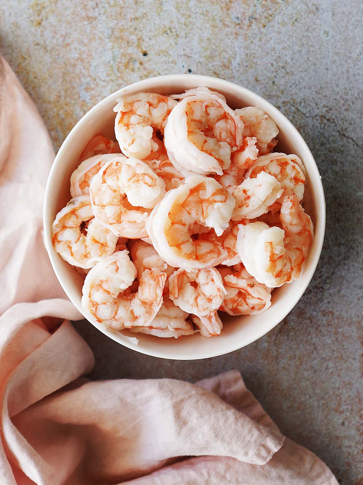 A white bowl with cooked shrimp and a pink fabric napkin on the side.