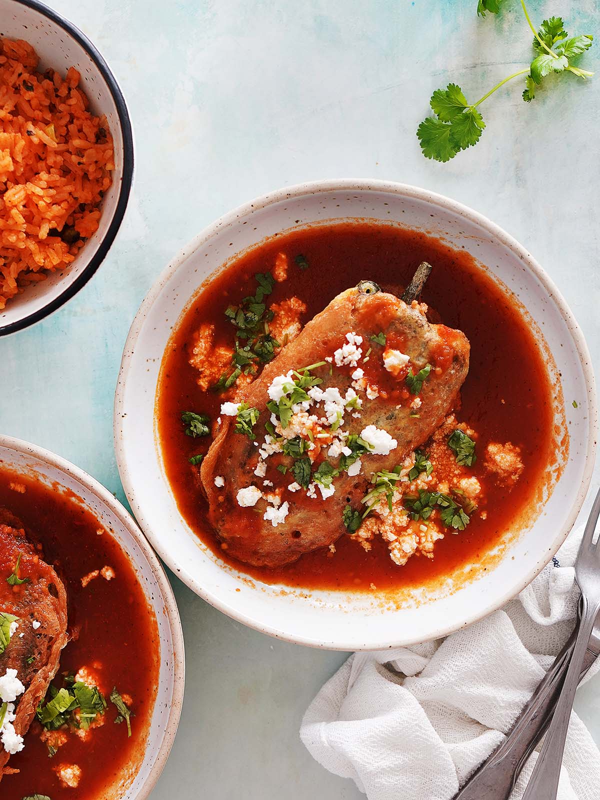 Two chiles Rellenos on a wide bowl with tomato sauce on the bottom.