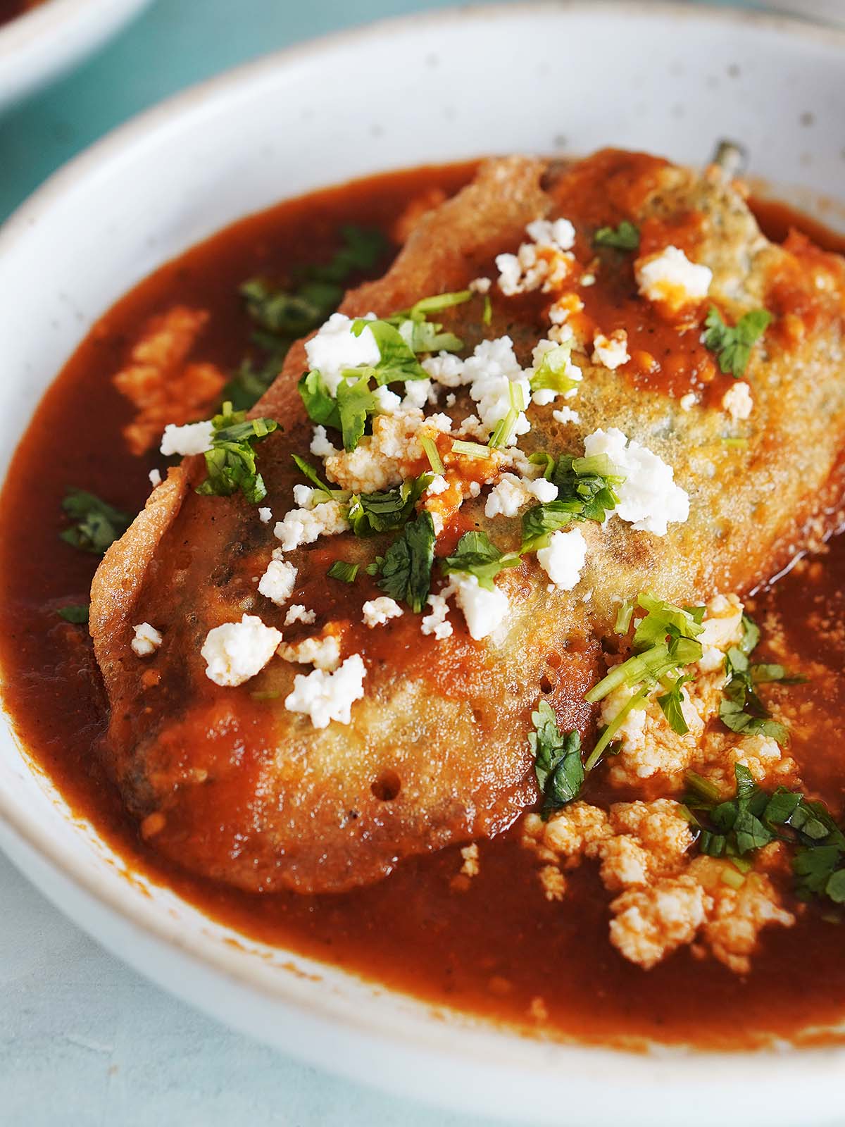 A chili relleno on a wide bowl with tomato sauce on the bottom.