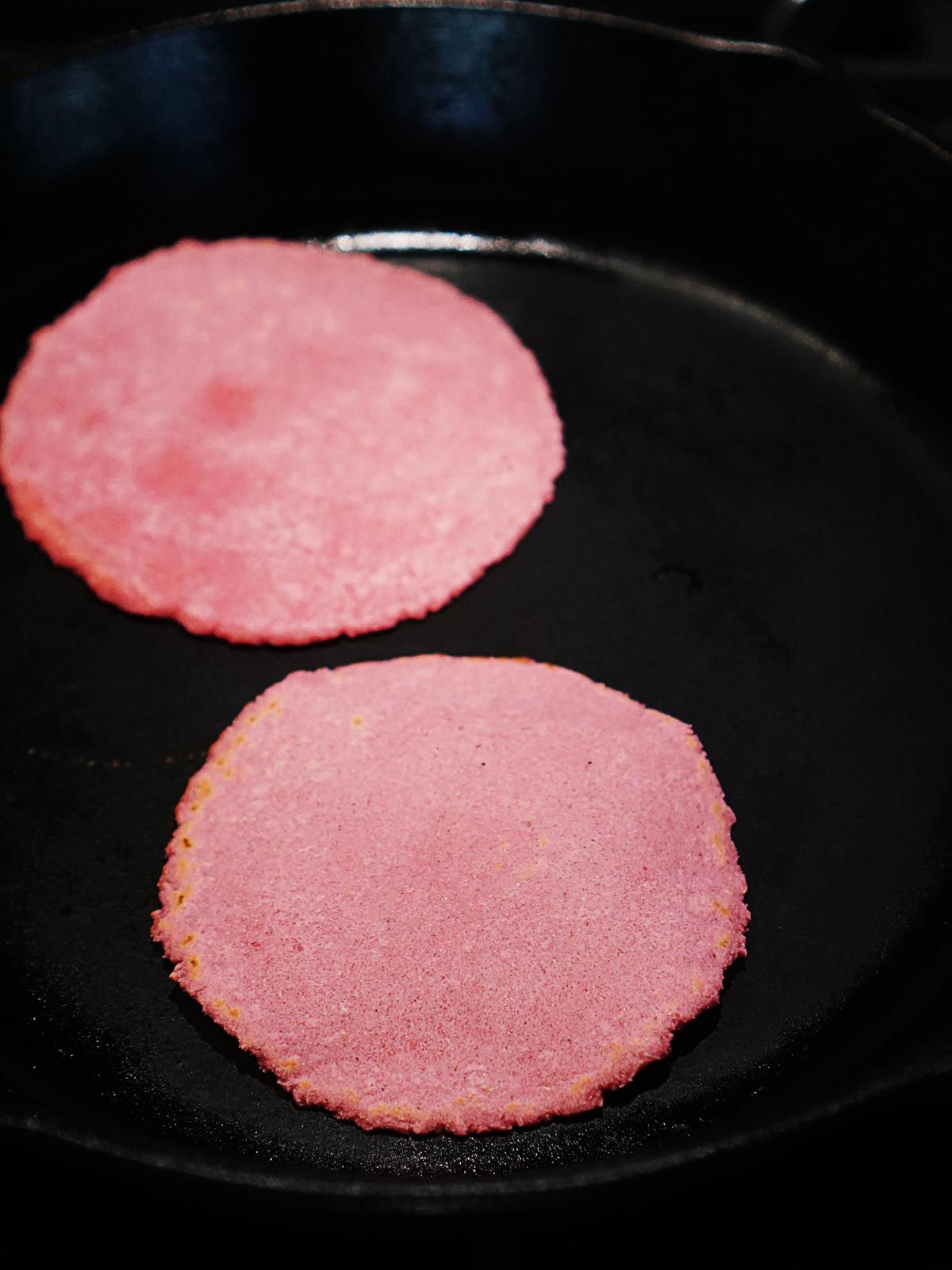 Cooking two pink tortillas on an iron skillet.