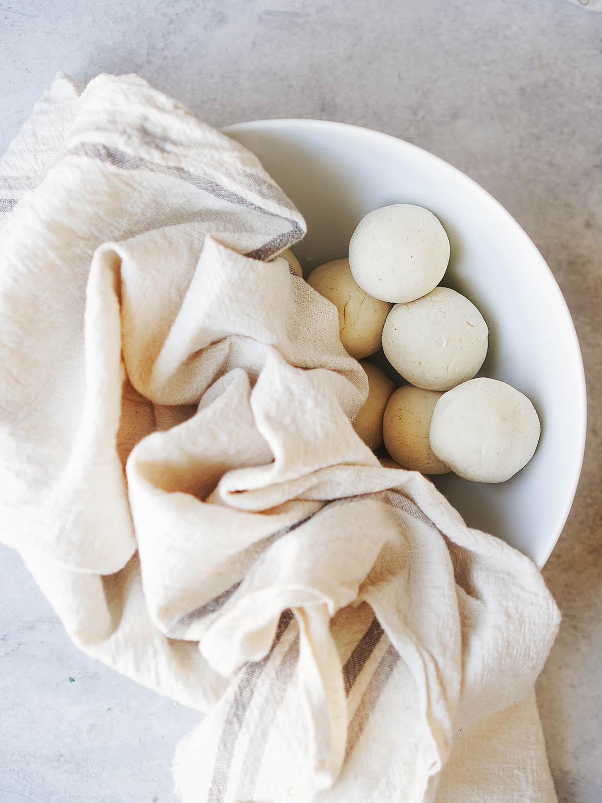 Tortilla dough balls in a white bowl covered with a kitchen towel.