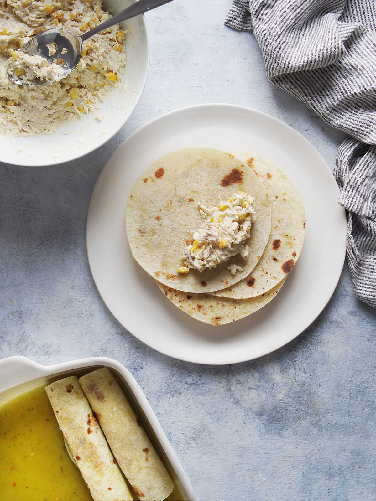 Filling tortillas with a creamy chicken mixture and then rolling them into a taquito shape.