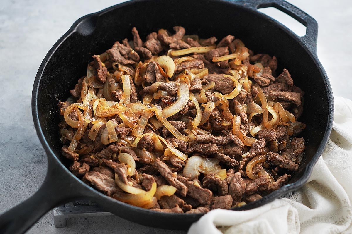 A skillet with cooked sliced onions and sliced steak.