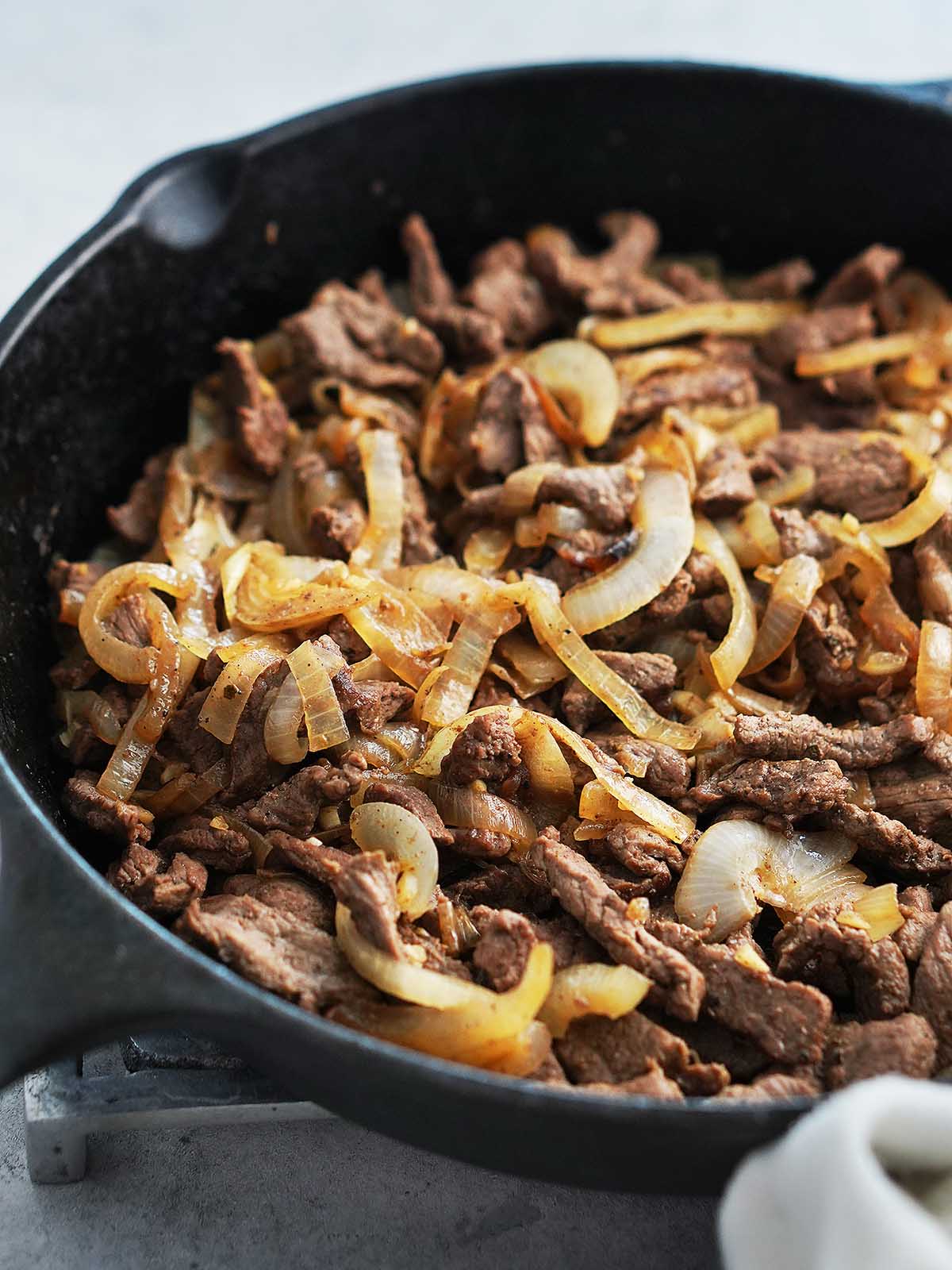 A skillet with cooked sliced onions and sliced steak.