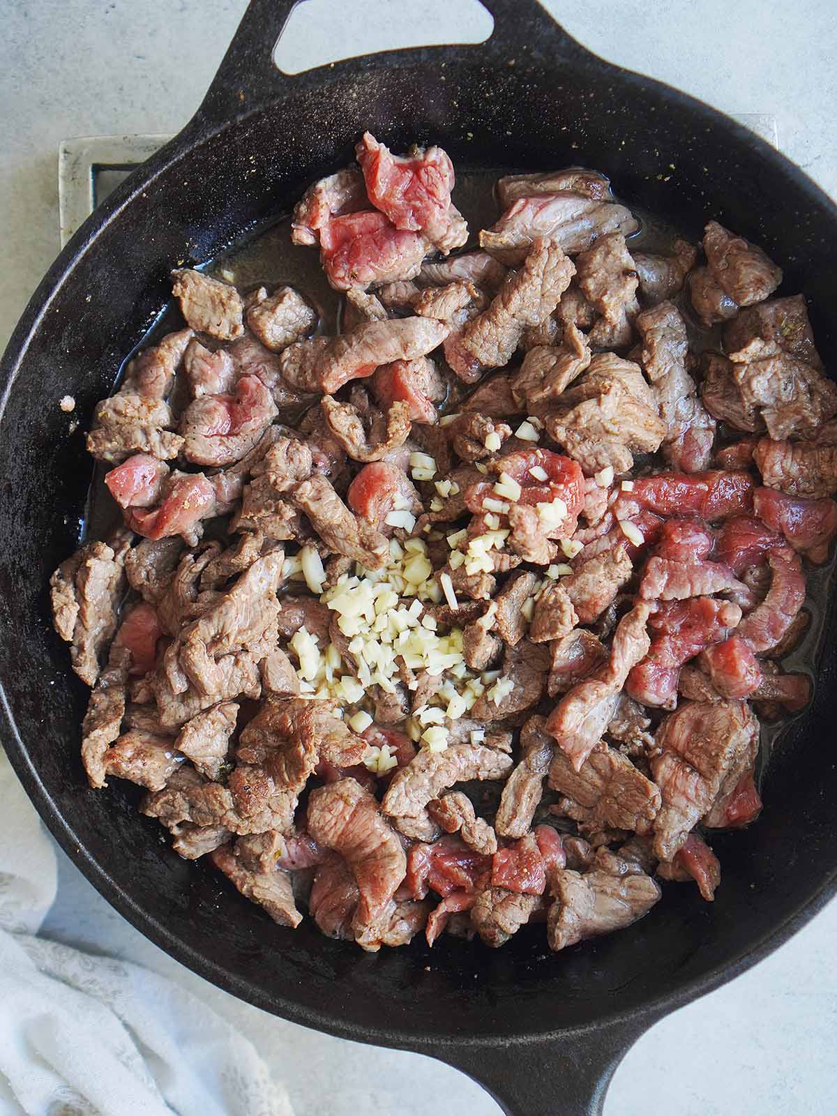 Cooking steak with chopped garlic in a skillet.