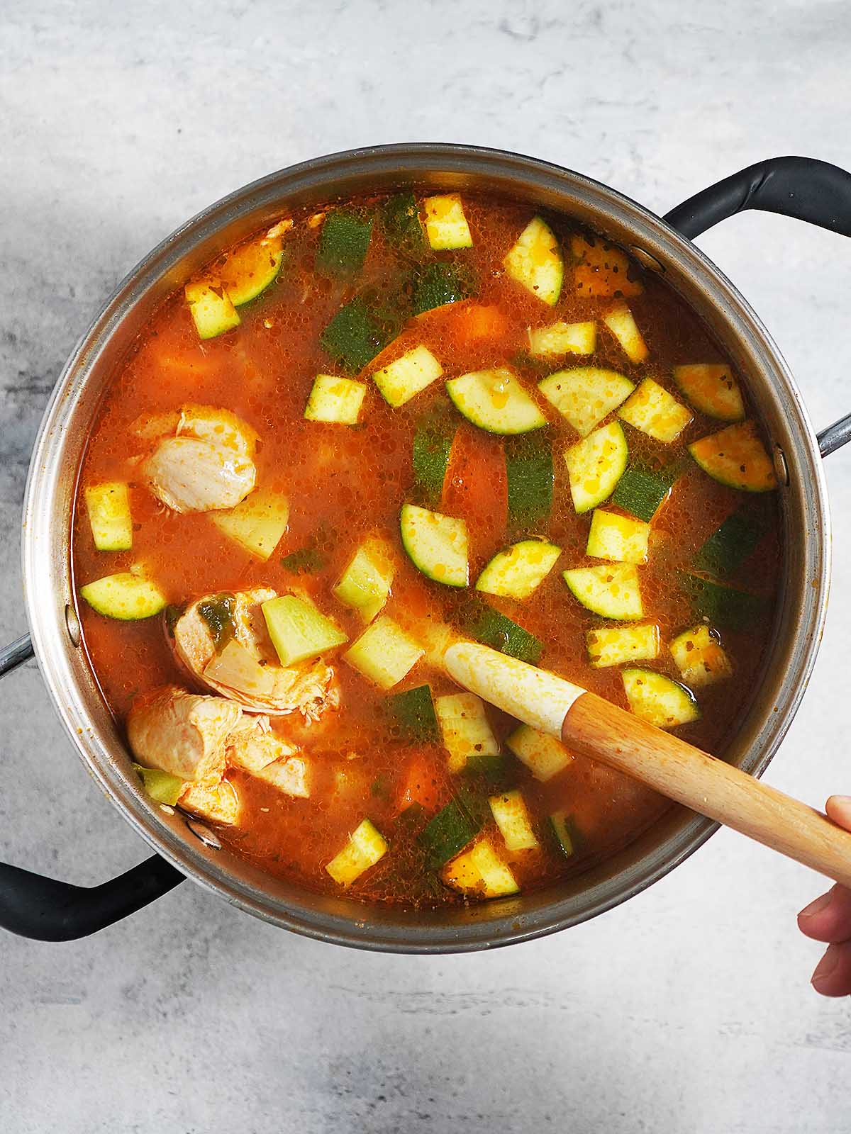 A large pot with caldo de pollo and a cooking spoon.