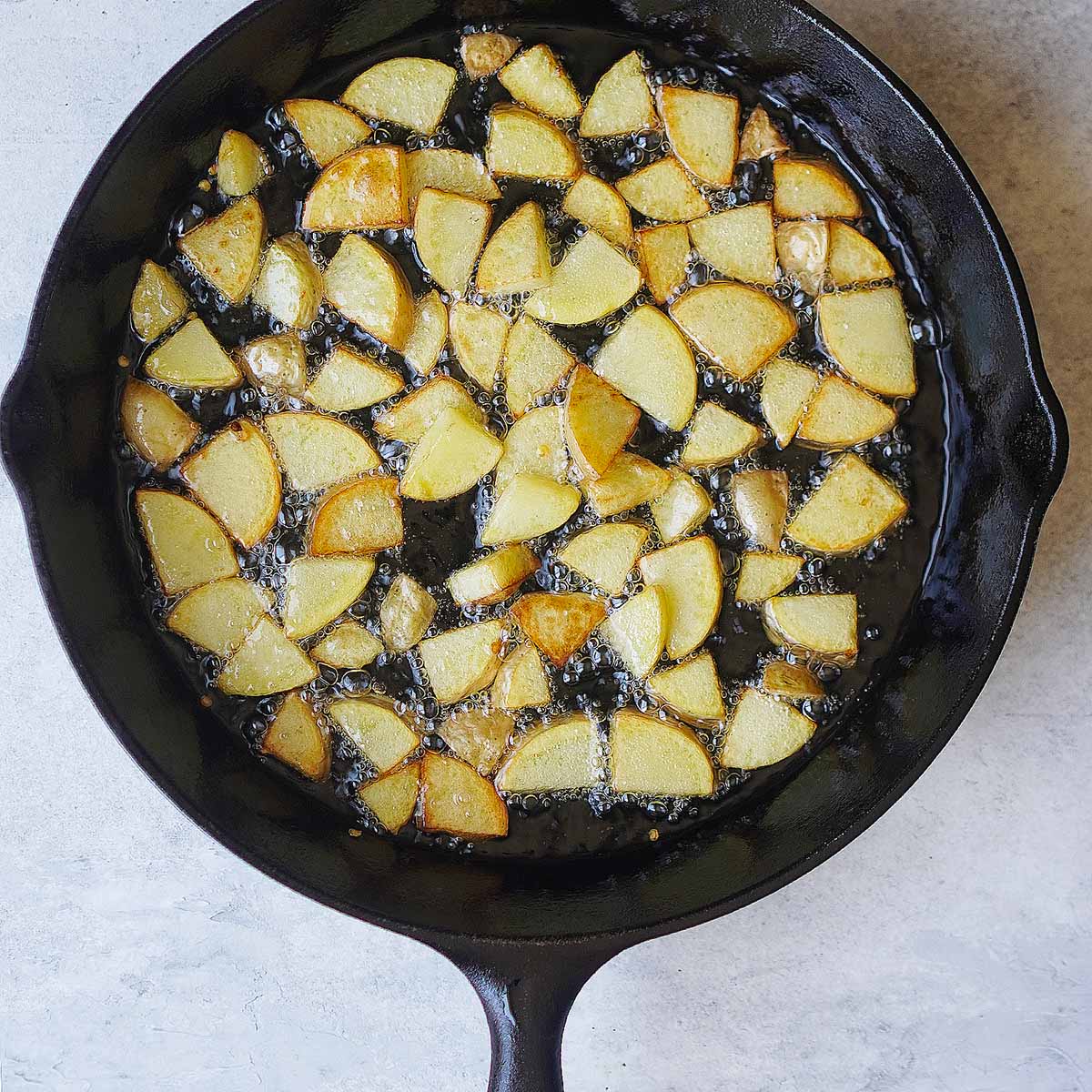 Frying potato slices in an iron skillet.