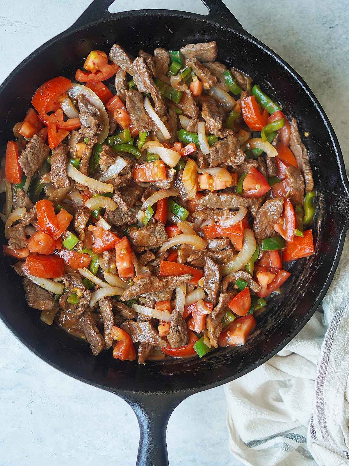 A skillet with cooked beef, onions, chiles & tomatoes.