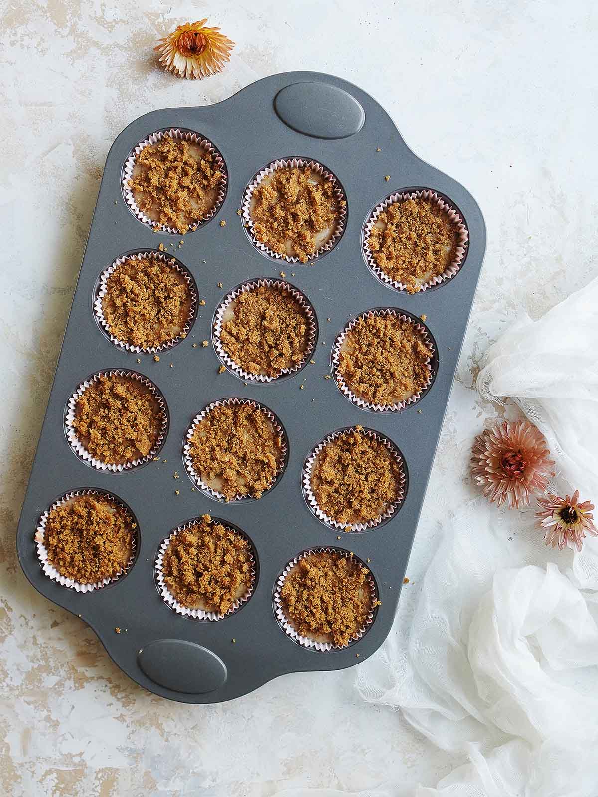 A 12 muffin pan showing the cinnamon crumbs on top of the batter.