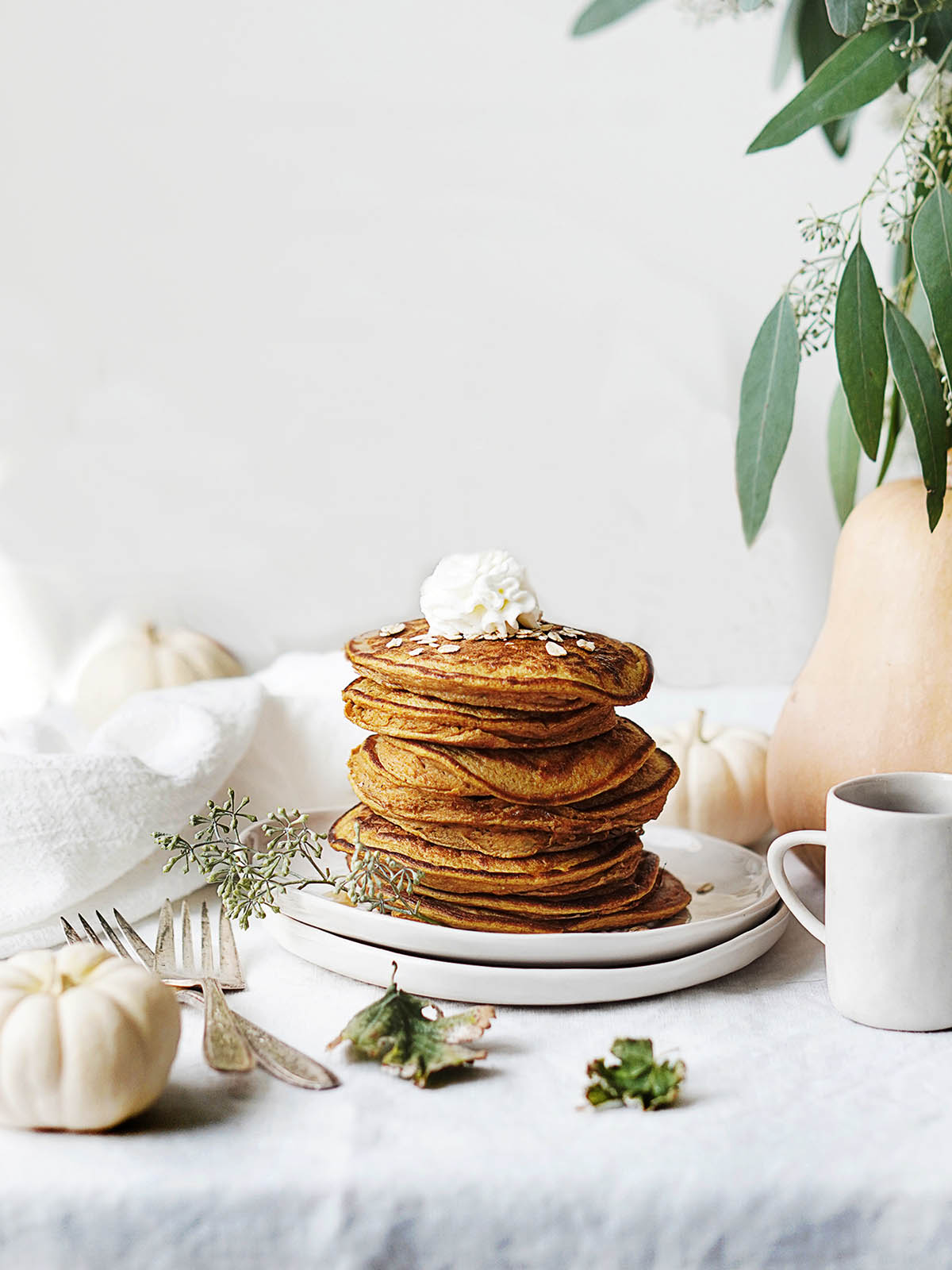 A stack of pumpkin protein pancakes on a table with a pumpkin next to it.
