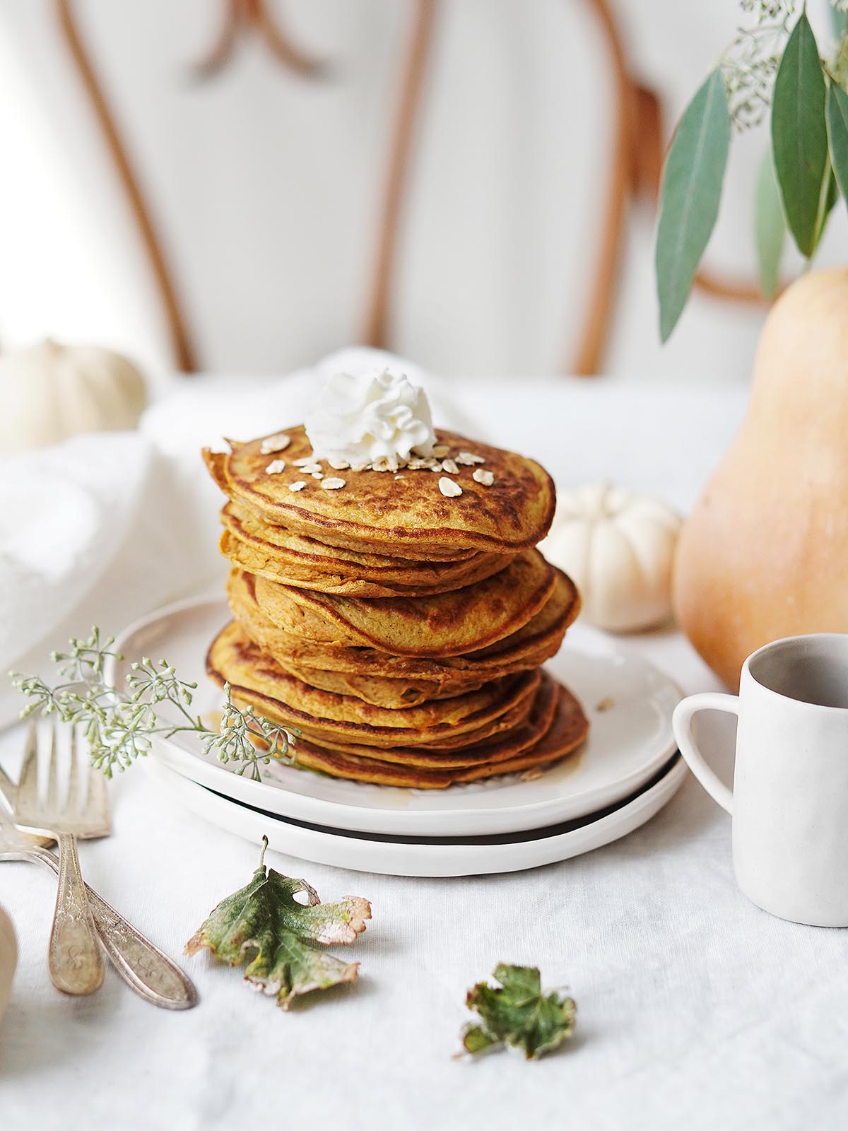 A stack of pumpkin protein pancakes on a table with a pumpkin next to it.
