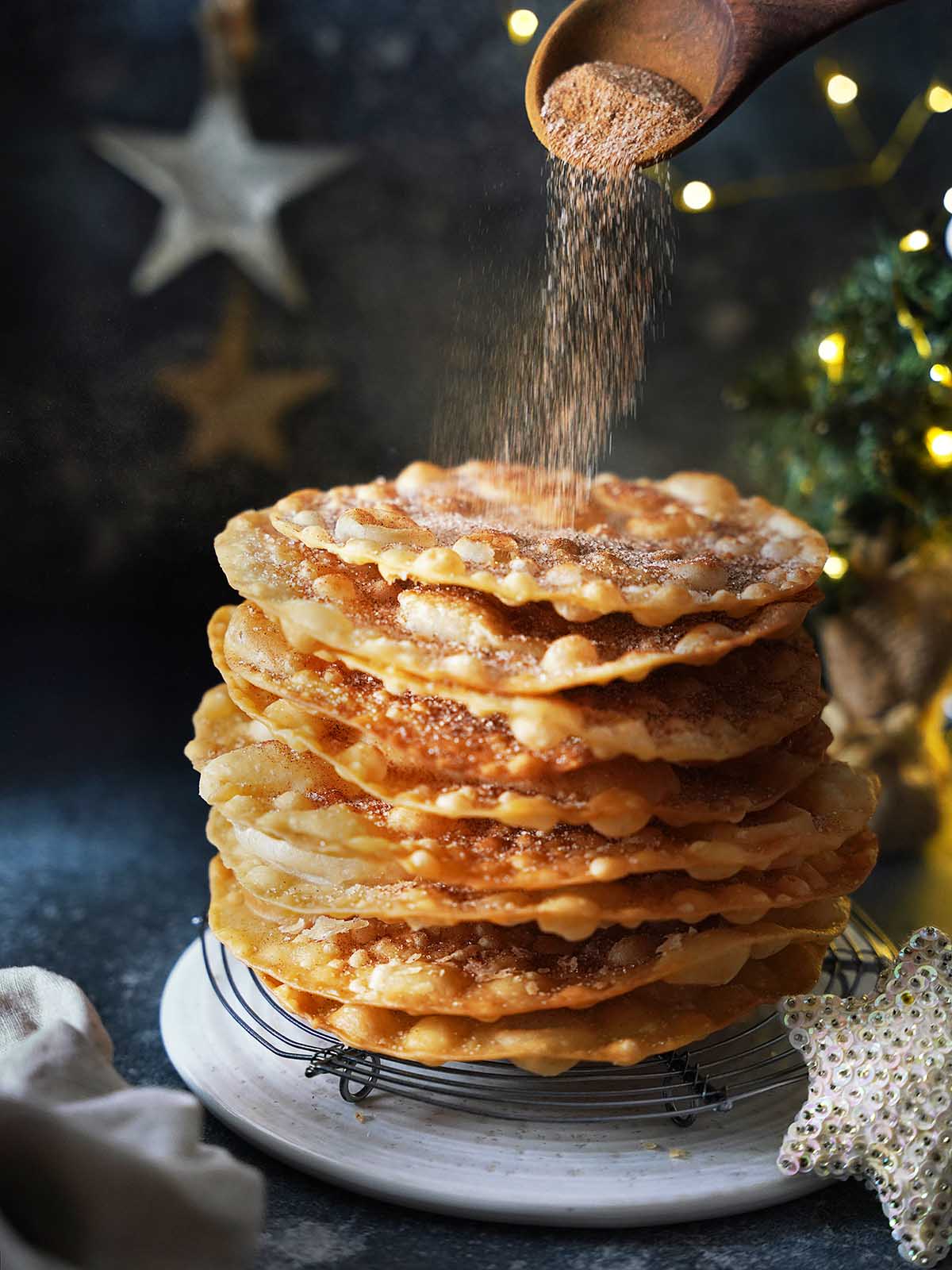 A stack of buñuelos on a white plate being sprinkled with cinnamon sugar.
