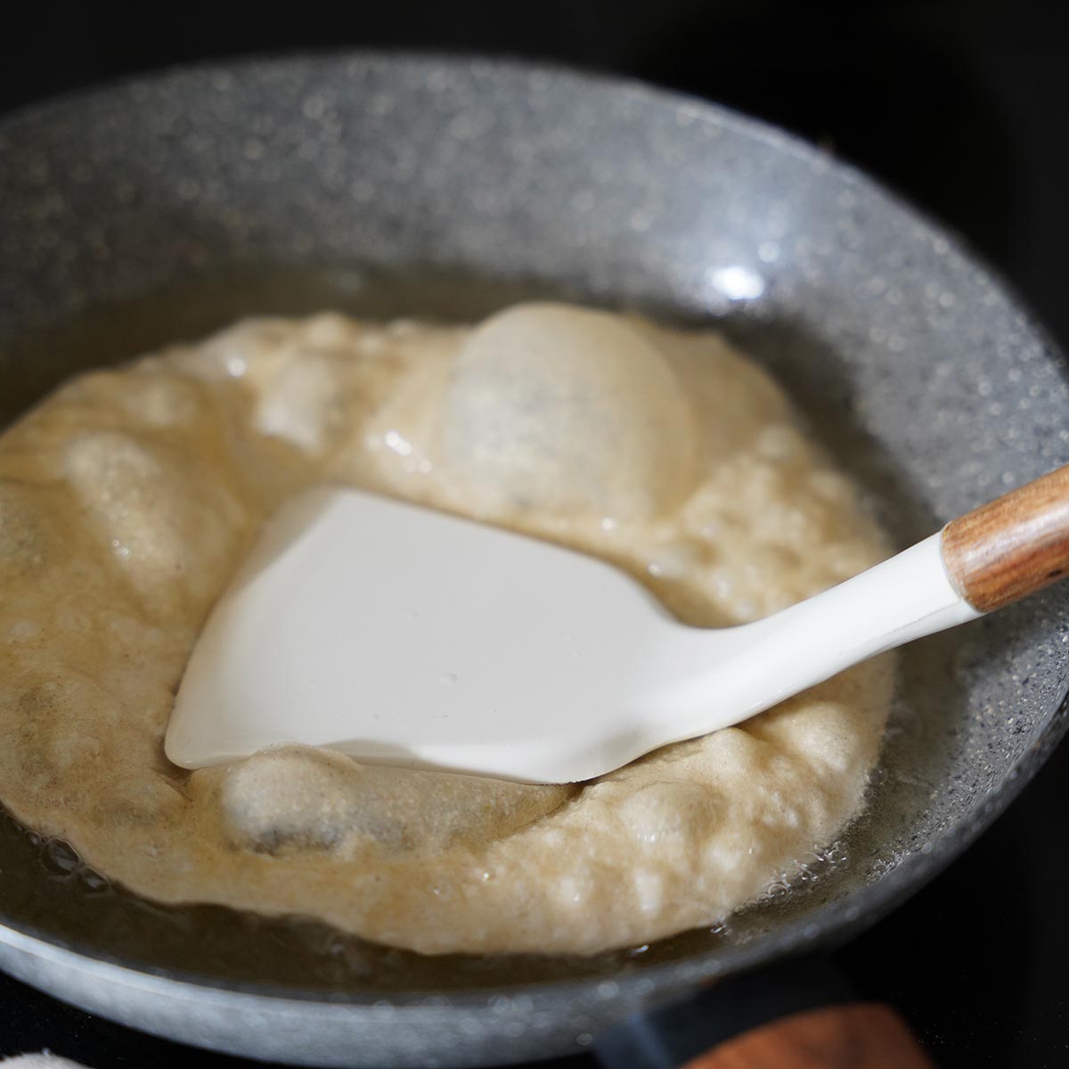 Frying the flattened dough in hot oil. A spatula pressing it down while it fryes.