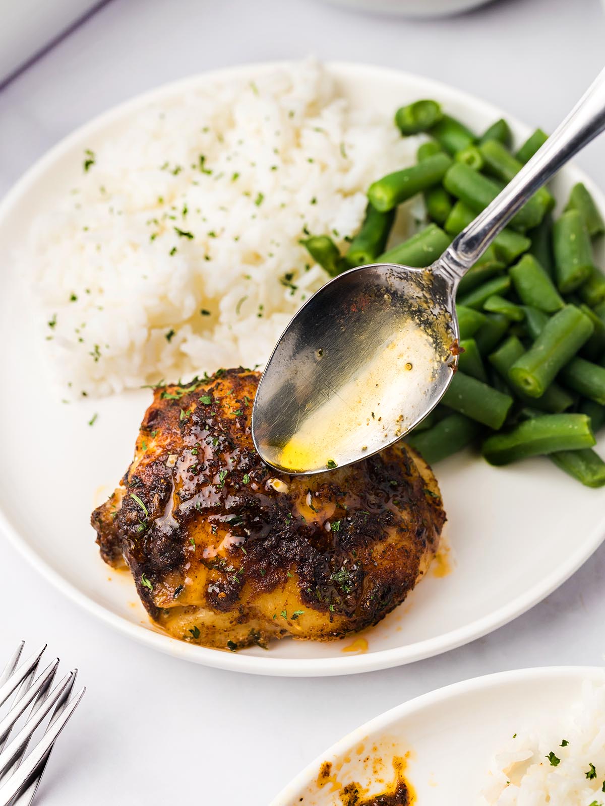 A baked chicken thigh with white rice and green beans on a white plate.