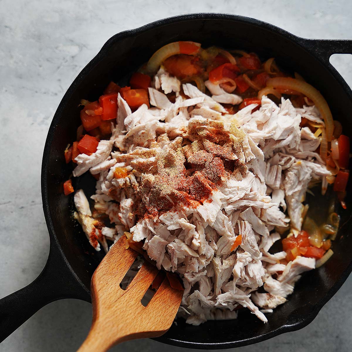 Sauteing shredded turkey with onions and tomatoes with spiced added on top.