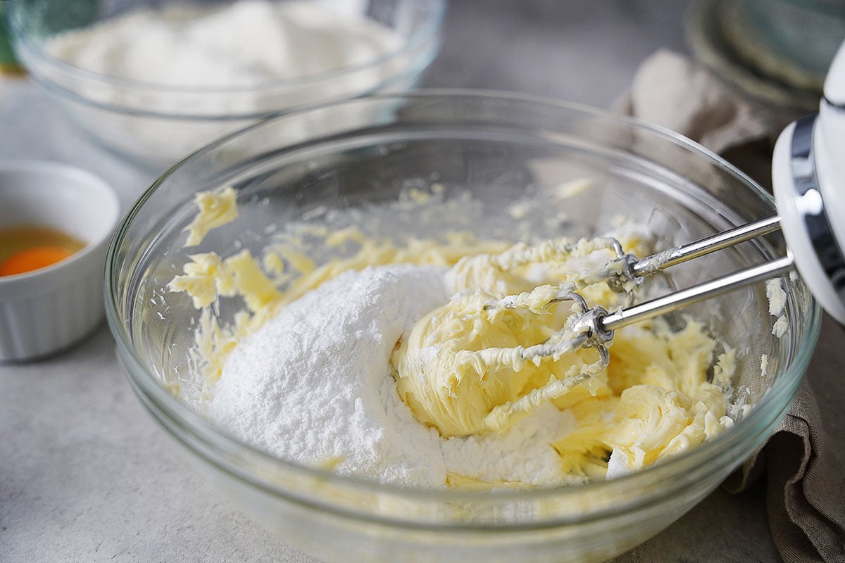 Adding confectioners sugar to the bowl with the creamed butter.