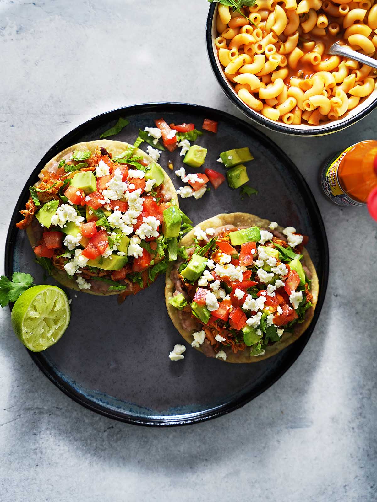 Two chicken tostadas on a plate topped with beans, shredded chicken, tomatoes, avocados and lettuce.