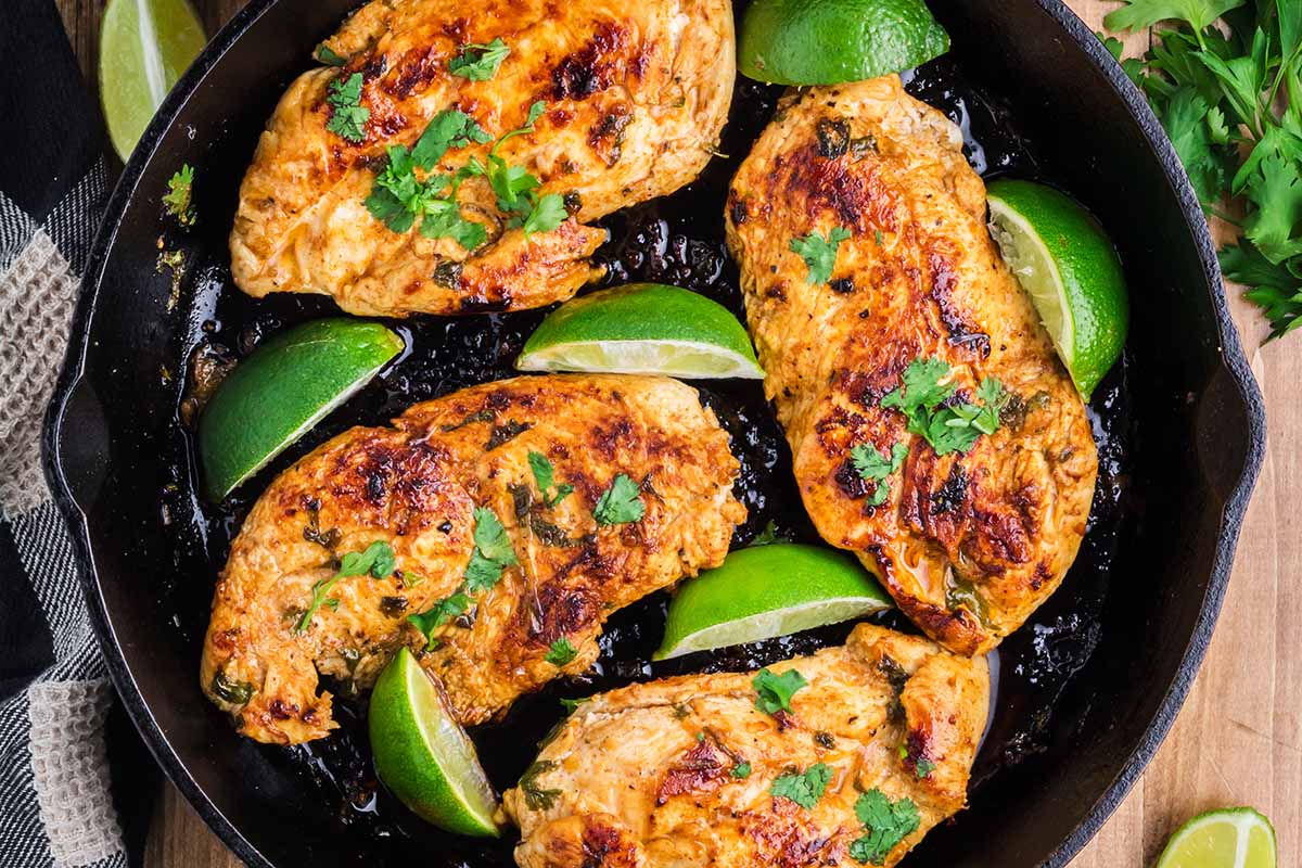 A skillet with cooked chicken breast with lime wedges as garnish.
