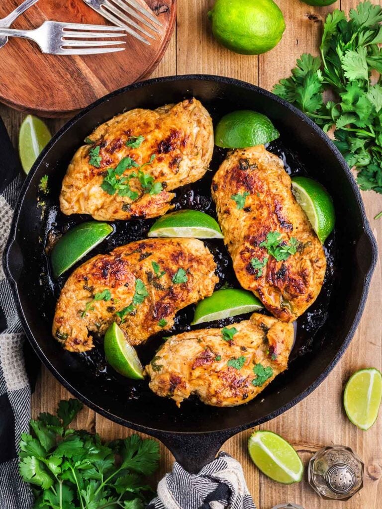A skillet with cooked chicken breast with lime wedges as garnish.