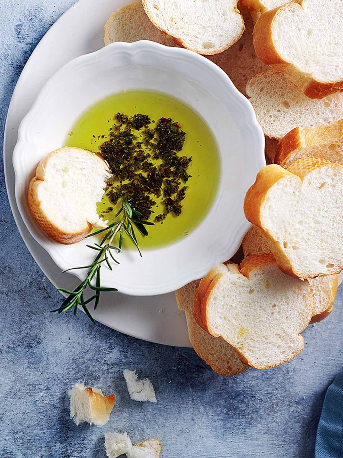 A bowl with oil and herbs and sliced bread on the side.