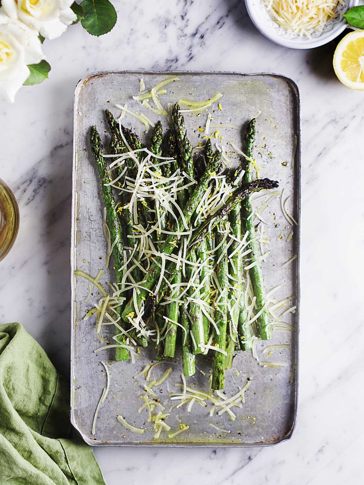 Asparagus placed on a metal tray sprinkled with shredded parmesan cheese.
