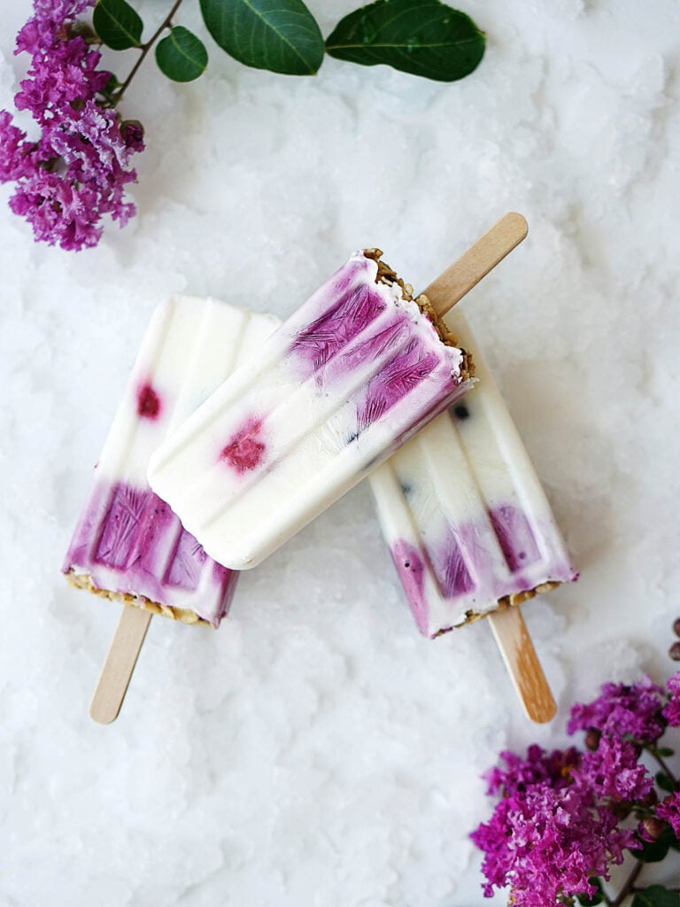Three Yogurt Berries Popsicles on a whiteboard with crushed ice on the bottom.