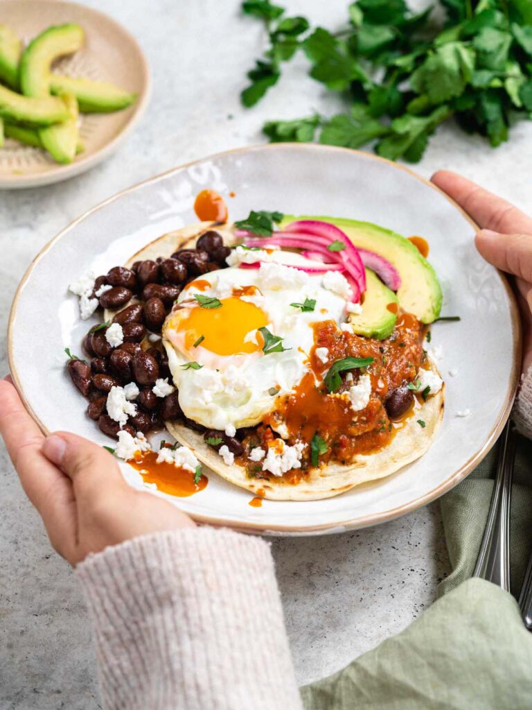 Two hands holding a plate with huevos rancheros.