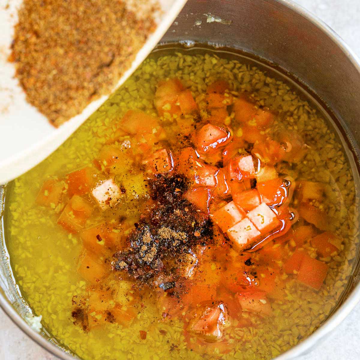 Adding the grinded spices to the pot with garlic, oil and tomatoes.