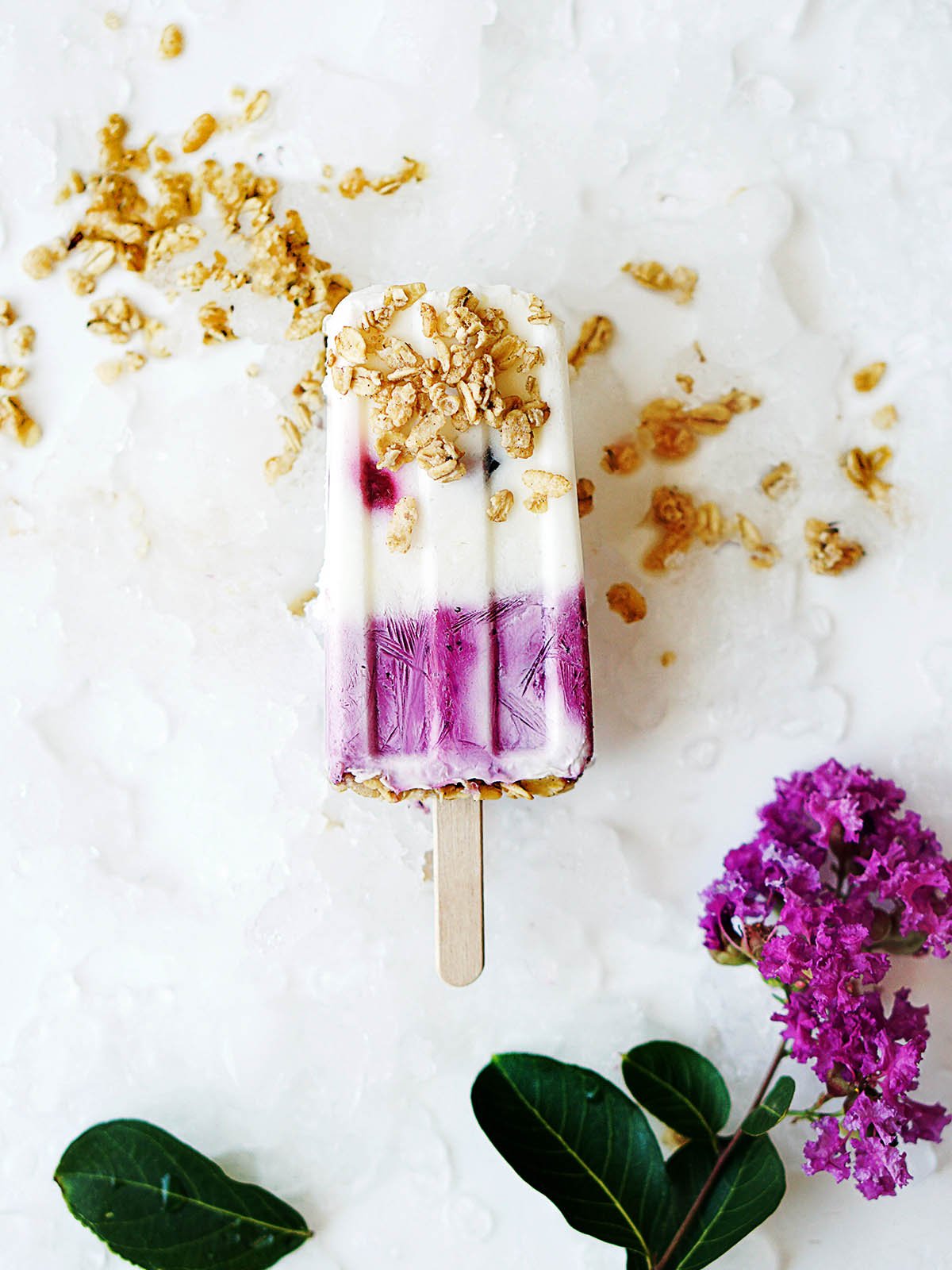 One Yogurt Berries Popsicle on a whiteboard with crushed ice on the bottom.