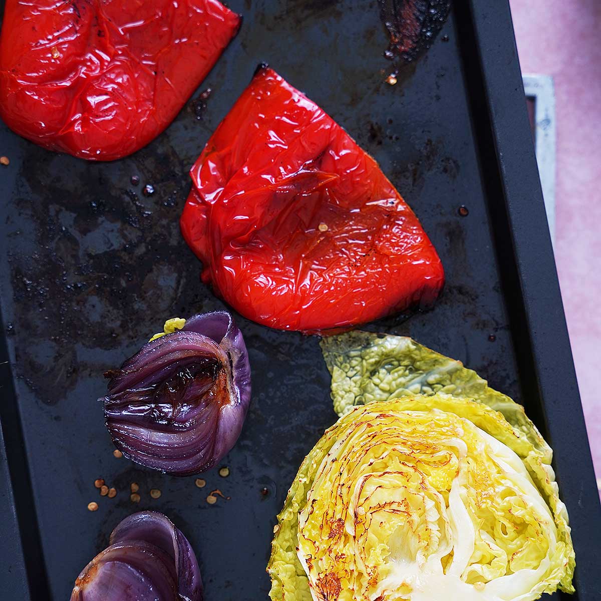 Roasted bell pepper, purple onion and cabbage on a baking tray.