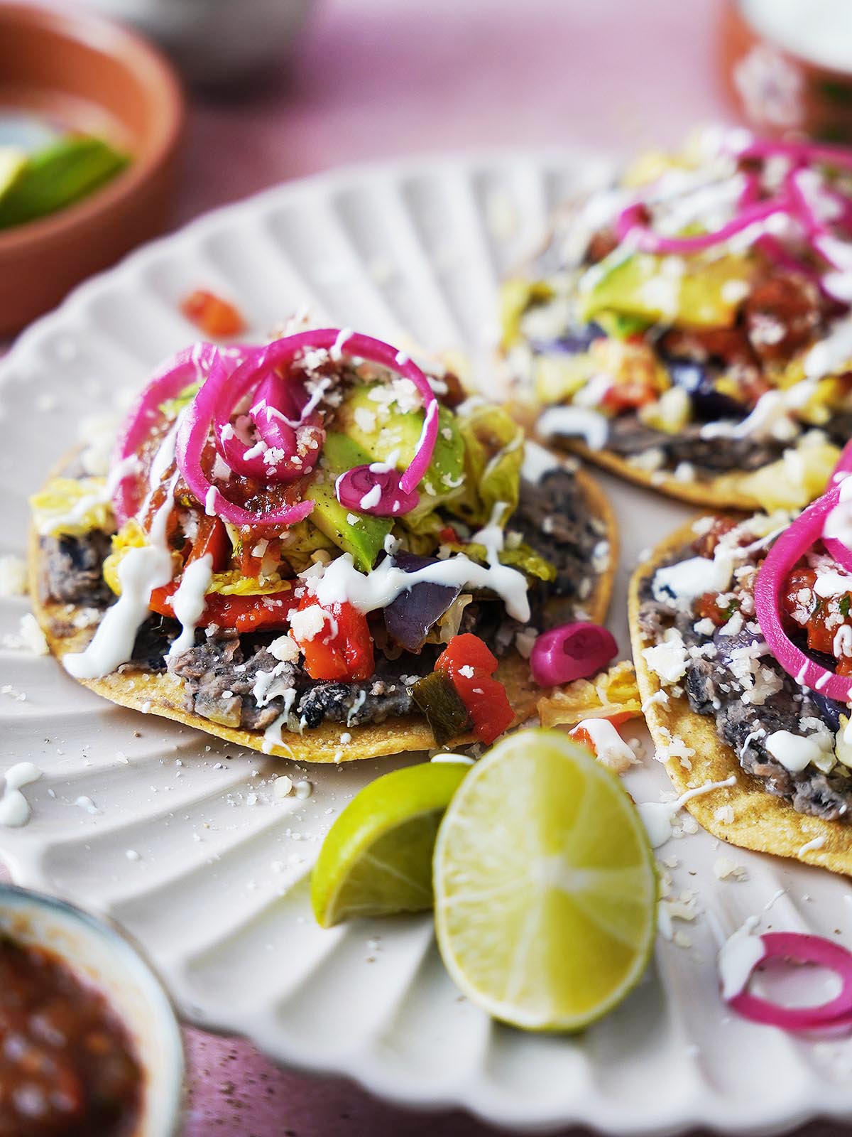 Three black bean tostadas topped with veggies and cheese on a plate.