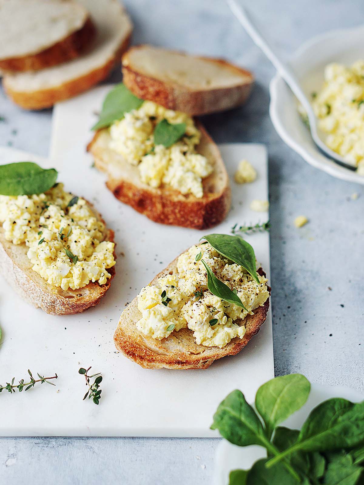 Two small toasts topped with egg salad and garnished with spinach leaves.