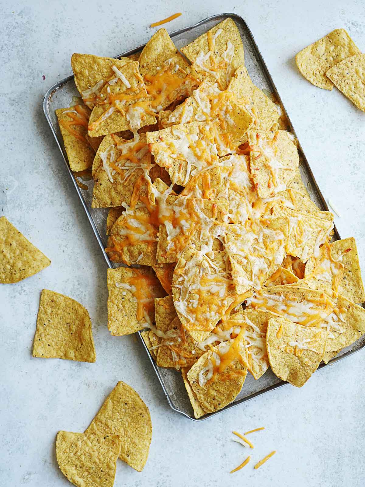 A baking tray with tortilla chips baked with melted cheese.
