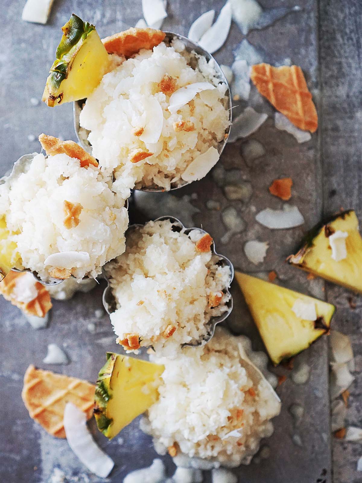 Four little metal tins with pineapple granita topped with shaved coconut.