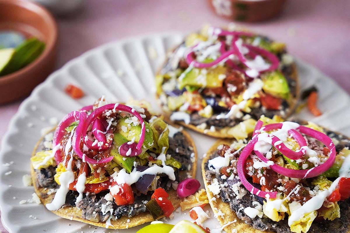 Three black bean tostadas topped with veggies and cheese on a plate.