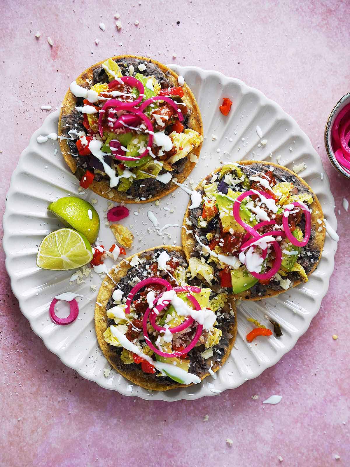 Three black bean tostadas topped with veggies and cheese on a plate.
