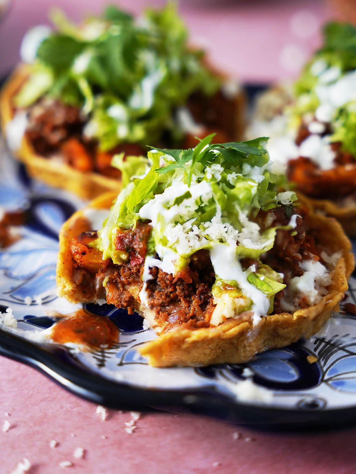 Three mexican sopes topped with chorizo and lettuce on a plate.