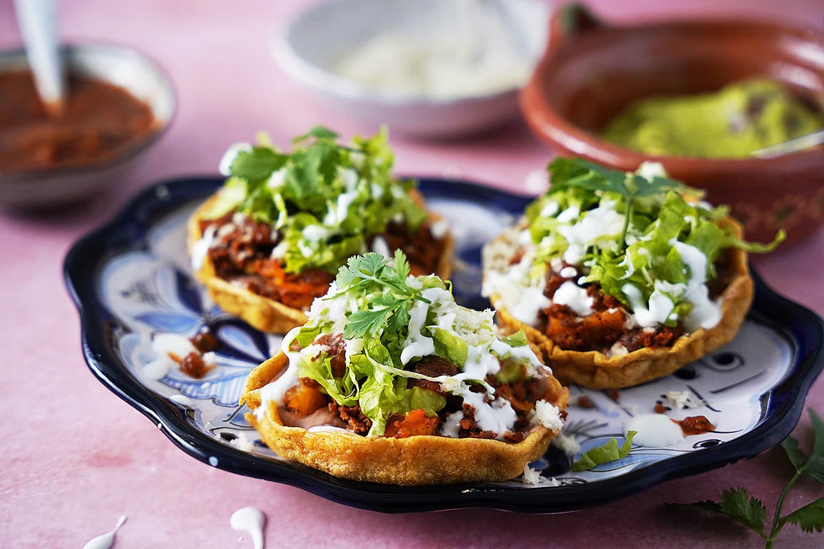 Three mexican sopes topped with chorizo and lettuce on a plate.