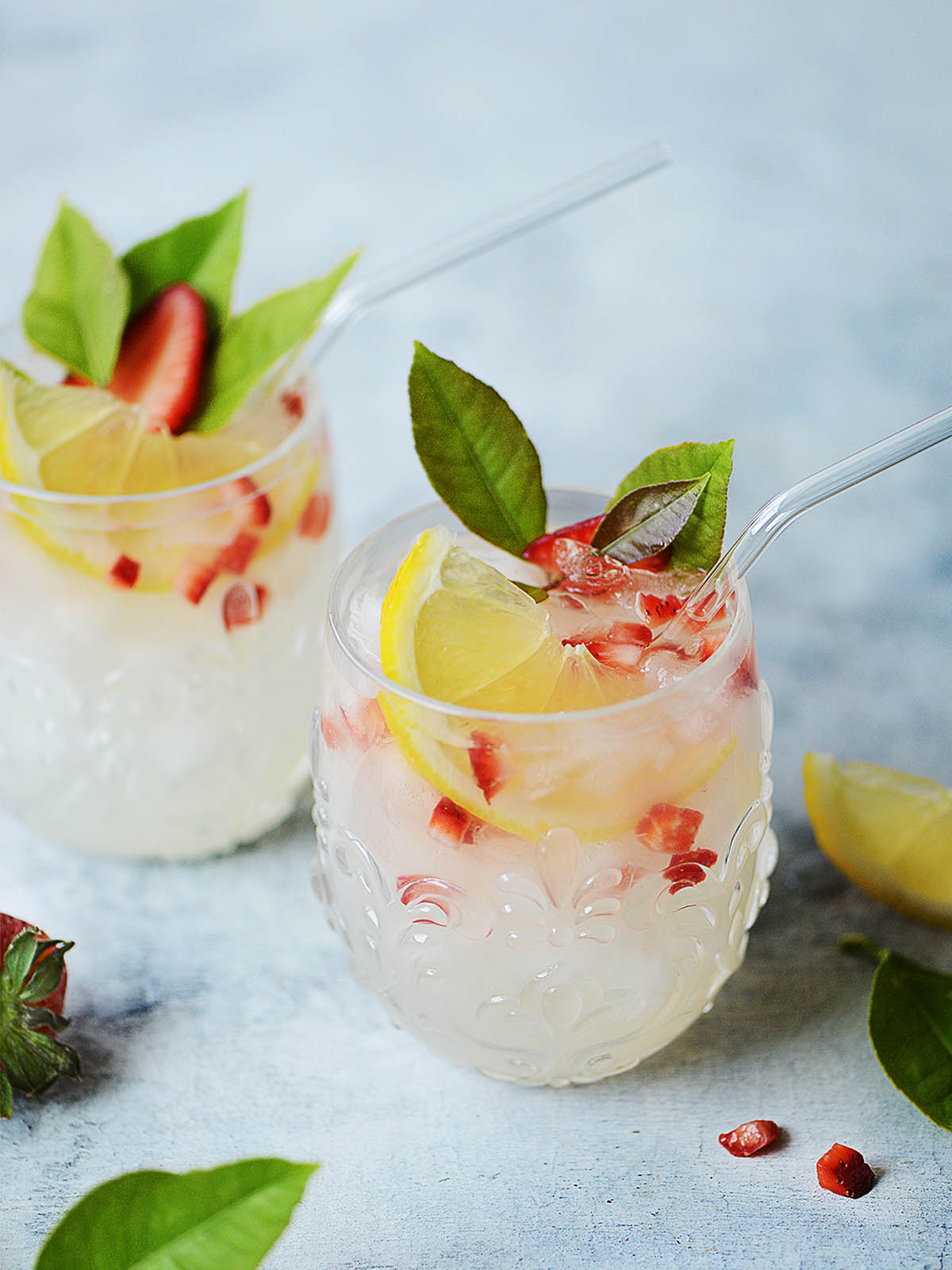 Two glasses with lemonade garnished with chopped strawberries.