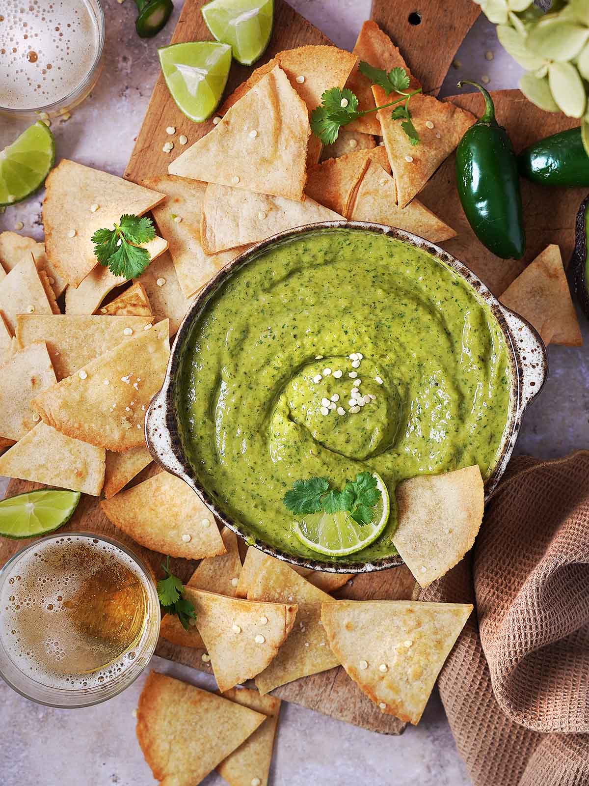 Creamy Jalapeno Salsa with Avocado in a brown bowl garnished with a slice of lime and cilantro leaves with tortilla chips around the bowl.