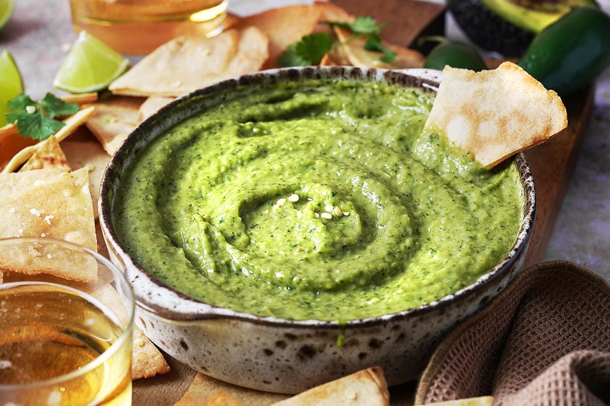 Creamy Jalapeno Salsa with Avocado in a brown bowl with tortilla chips on the side.