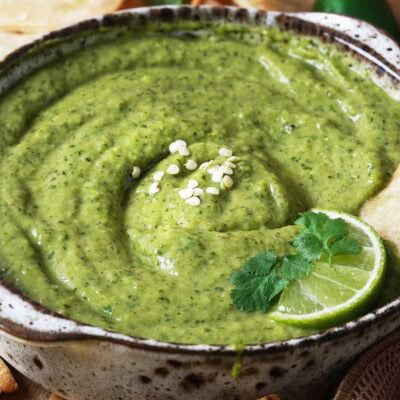 Creamy Jalapeno Salsa with Avocado in a brown bowl garnished with a slice of lime and cilantro leaves.