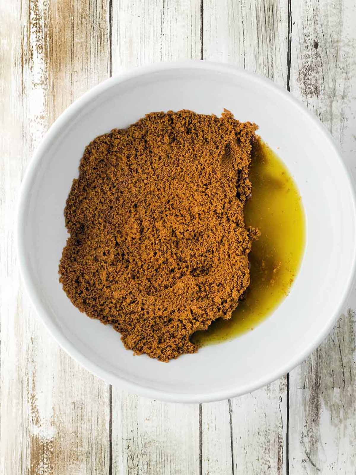 Cookie crumbs in a white bowl with melted butter.