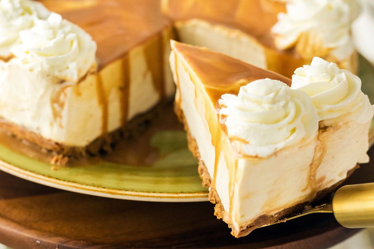 A slice of Dulce De leche cheesecake on a cake serving spoon with whipped cream topping on top.