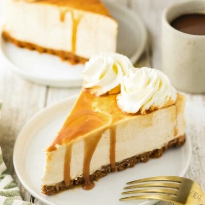 Rich and creamy caramel cheesecake with whipped cream topping on a white plate.