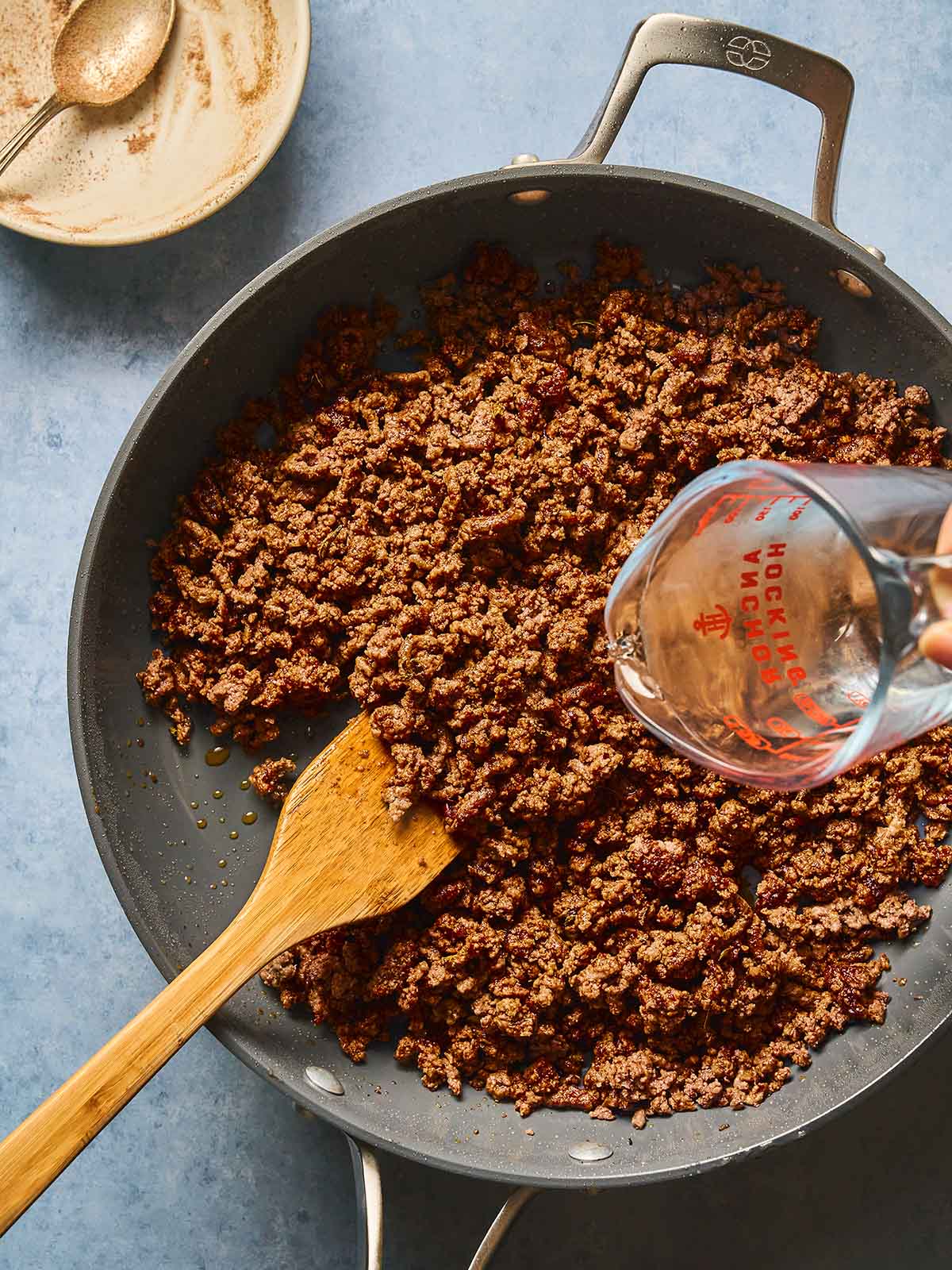 Adding water to the cooked ground beef in a skillet.